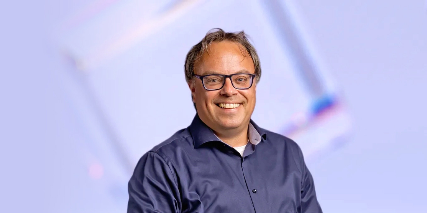 Portret van lachende Reinoud Pauwels van Ondernemingsjuristen in donkerblauwe bloes tegen lichtpaarse achtergrond
